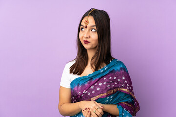 Young Indian woman isolated on purple background having doubts while looking up