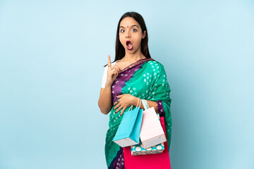 Young Indian woman with shopping bags thinking an idea pointing the finger up