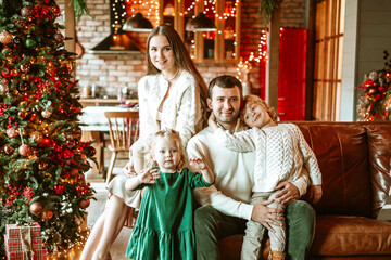 family of four parents pregnant mom and dad and two siblings little boy and girl in stylish clothes in chalet are ready to welcome Christmas and New Year near Christmas tree with gift box presents