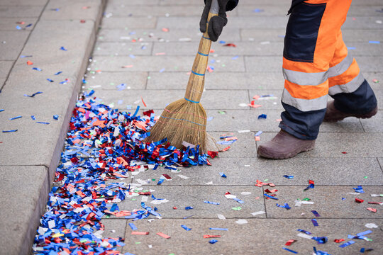 A janitor cleans up colorful confetti with a broom on the side of a city street after a celebration event