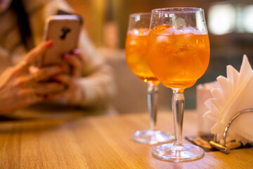 evening coctail with friend. two coctail glasses on table in restaurant, faceless woman typing in blur