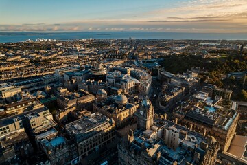 Fototapeta na wymiar Aerial view of Edinburgh as sun rises over the city. Old city wakes up with the sunrise. Early morning haze lifts as the first rays of sunlight hit the city of Edinburgh, Scotland
