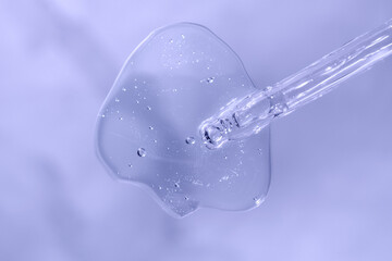 Pipette with fluid hyaluronic acid on violet blue background. Cosmetics and healthcare concept closeup. Dose of serum or retinol with air bubbles. Luxury gel or beauty product presentation in macro