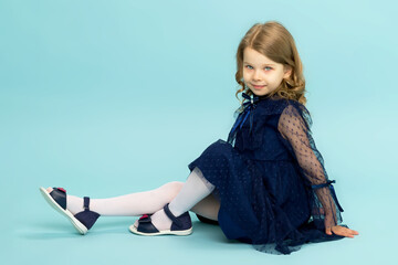 Happy little girl in blue dress sitting on floor