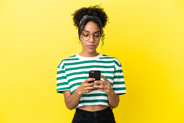 Young african american woman isolated on yellow background using mobile phone