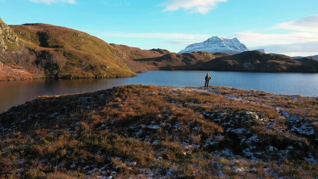Woman in Scottish Tartan gazing into the mountains of the Scottish Highlands next to a loch (aerial shot)