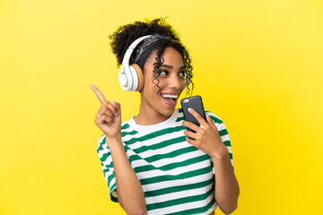 Young african american woman isolated on yellow background listening music with a mobile and singing