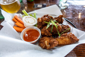 Close up of deliciously golden and fried chicken wings in a basket, next to cups of ranch and hot sauce