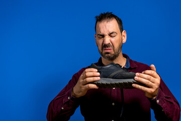A man hold sneaker in his hands. Nasty smell. Stink legs, fungus on the legs. - obrazy, fototapety, plakaty