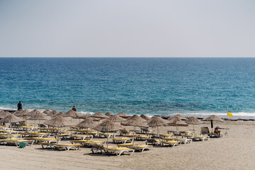Fototapeta na wymiar View on empty sandy beach with fern beach umbrellas and blue clear water during calm day. Mediterranean sea, Alanya, Turkey.