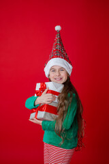 Portrait of a joyful child with a gift. Elf girl with gifts, Santa Claus helper on a bright red bright colored background. 