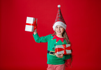 Portrait of a joyful child with a gift. Elf girl with gifts, Santa Claus helper on a bright red bright colored background. 