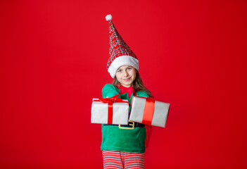 Portrait of a joyful child with a gift. Elf girl with gifts, Santa Claus helper on a bright red bright colored background. 