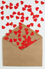 red paper hearts fall out of a craft envelope on a white background