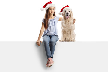 Girl hugging a labrador retriever dog with christmas santa claus hat, seated on a blank panel