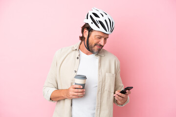 Senior dutch man with bike helmet isolated on pink background holding coffee to take away and a...