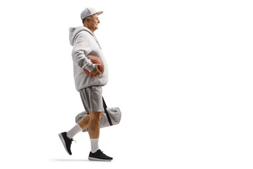 Full length profile shot of a mature man walking with a basketball and a sports bag