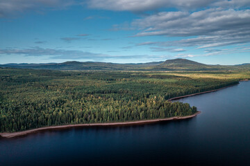 Green forest and lakeshore at Lake Siljan from above with blue sky in Dalarna, clouds in sky, Sweden.