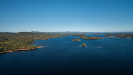 Green forest and lakeshore with islands at Lake Siljan from above with blue sky in Dalarna, clouds...
