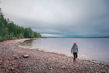 Woman walking at beach and lakeshore with forest at Lake Siljan in Dalarna, Sweden. - 474283968