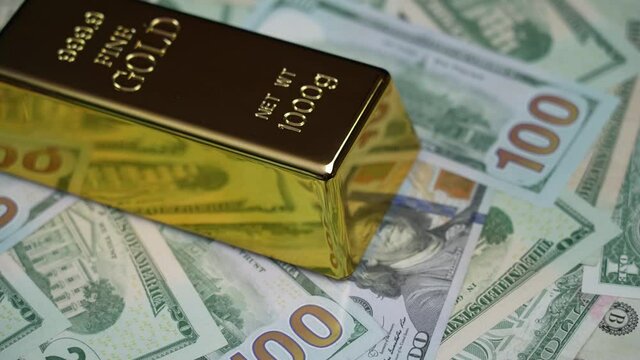 A gold bar rotates above US fiat currency.	