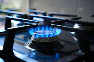 Blue flame from gas hob produce greenhouse gas emissions. Kitchen stove grate on a burner fuelled...