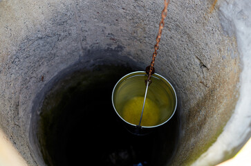 Metal bucket in draw-well in European village. Retro stone water well in rural area