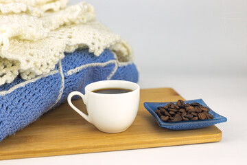 A cup of coffee, a knitted plaid, coffee beans in a saucer, a wooden tray on a white background. 