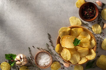 Chips, potato crisps heap with garlic, rosemary, in bowl on grey stone background. Junk food or fast food.