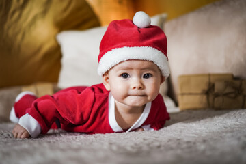 cute little newborn baby in christmas outfit with santa claus hat crawling on a couch in a cozy bright living room 