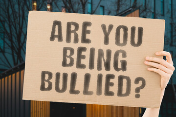 The question " Are you being bullied? " on a banner in men's hand with blurred background. Tired. Annoyed. Wild. competitive. Irate. irritated. Fighting. Ferocious. Fierce. Trouble. Nervous