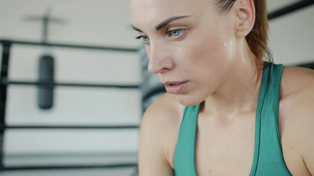 Tired fighter young woman is sitting in boxing ring corner breathing hard resting during break. Youth and sports activities concept.