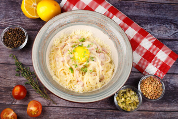 Traditional Italian pasta dish, spaghetti carbonara with yolk, parmesan cheese, bacon in plate on black rustic stone background, top view.