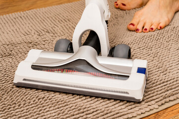 Close up of vacuum cleaner on the carpet with woman legs behind