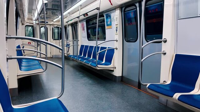 An empty subway car travels through a tunnel. No one sits on blue chairs.