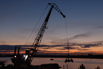 Fototapeta premium The silhouette of a construction crane at sunset against the river