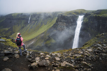 Obraz premium Woman with backpack and lilac jacket enjoying Haifoss waterfall of Iceland Highlands in Thjorsardalur Valley