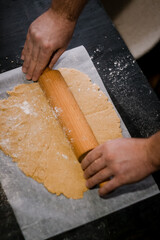 male hands roll gingerbread dough with a wooden rolling pin, close-up