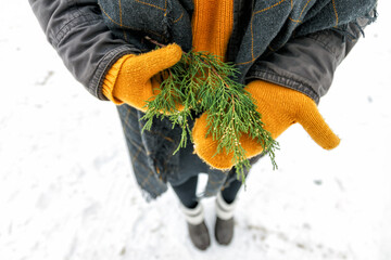 a young happy woman holds a cypress branch in yellow mittens in her hands. View from above.