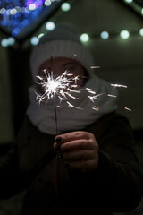young happy woman in a winter hat holds a sparkler in front of her