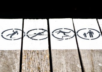 Warning signs spray paint in black and white on the boardwalk near waterside for No swimming, No jumping, Slippery surface and take care of your children.