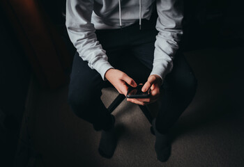 Close up of teen boy in white sweater texting on phone in dark.