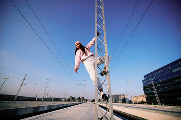 Rebellious teenage girl climbing on the metal construction at the train station.