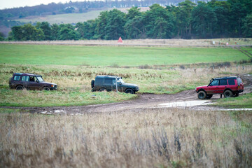 three Land Rover Discovery 4x4 off-road vehicle driving across mud, water-logged terrain and wading through deep water pools, Wilts UK. 