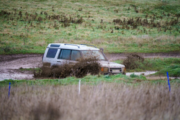 Land Rover Discovery 4x4 off-road vehicle driving across mud, water-logged terrain and through deep...