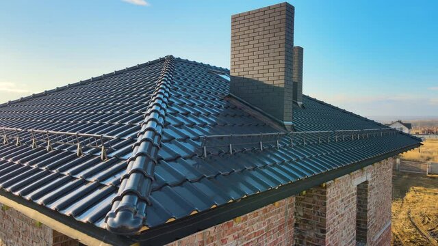 Closeup snow guard for safety in winter on house roof top covered with ceramic shingles. Tiled covering of building
