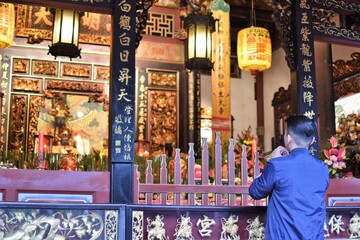 An Asian man prays at a shrine adorned with flowers and lanterns
