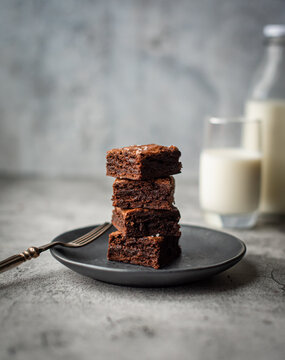 Stack of chocolate brownies on a plate with glass of milk.