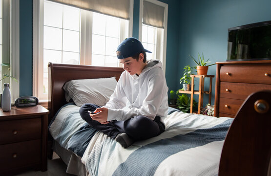 Teen boy in white hoodie on smartphone alone in his bedroom.