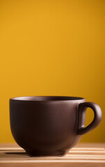 brown cup with coffee or chocolate on wood, with yellow background
